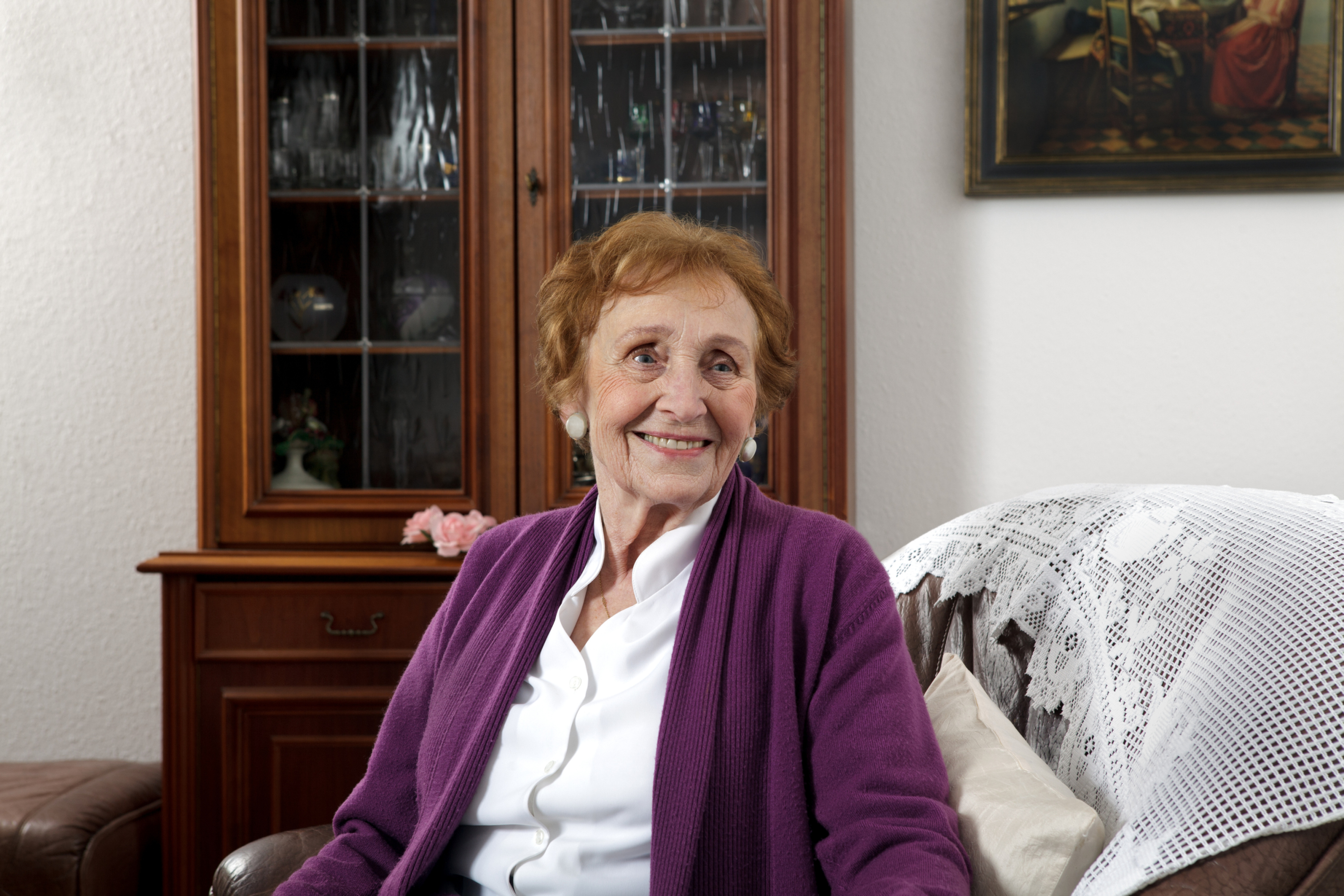 Eine alte Dame sitzt lächelnd auf dem Sofa in ihrem Wohnzimmer